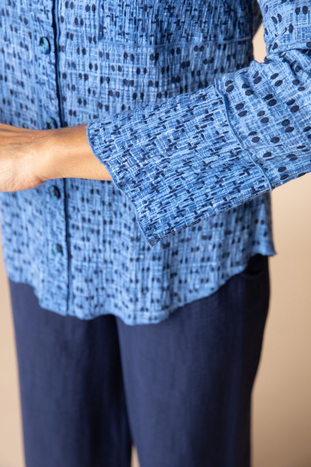 Woman wearing a blue patterned shirt and dark pants against a beige background