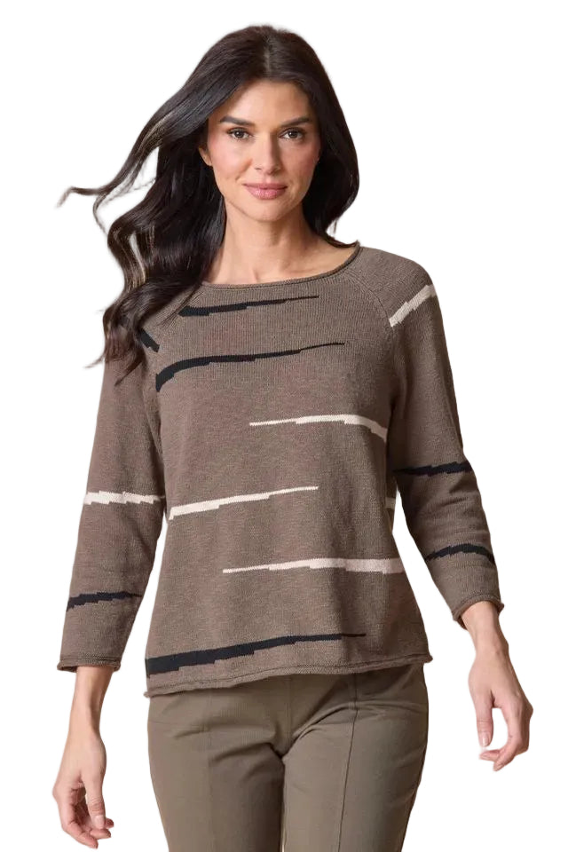 A woman modeling a brown knit sweater with horizontal black and white stripe patterns, paired with olive green pants, against a solid beige background.